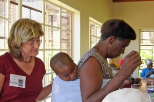 susan_grandchild_sewing Susan Fenner of Grannies à Gogo looks at a sleeping child on the back ofhis grandmother who is learning sewing skills taught by Beverley Barling.
