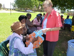 Volunteer Joy Burton (standing) helps the gogos with their various handicrafts. Here she discusses 88 year-old Inah Mashego’s crocheted bag. 